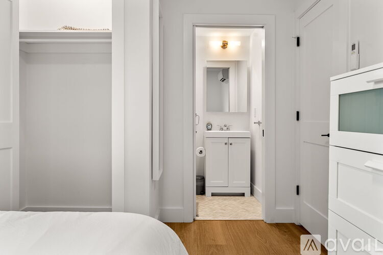 A white bedroom with a bed on the left and a bathroom with a sink and mirror on the right.