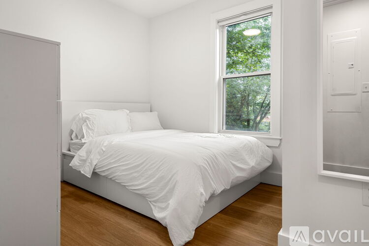 A bedroom with a white bed and a window showing greenery outside.