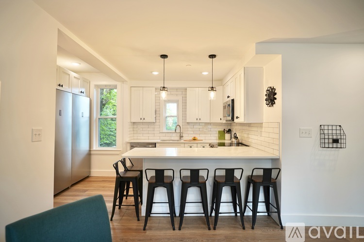 A kitchen with white cabinets and a white island with four black barstools.
