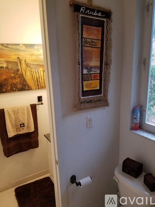 A bathroom with a towel hanging on the door and a picture of a beach on the wall.