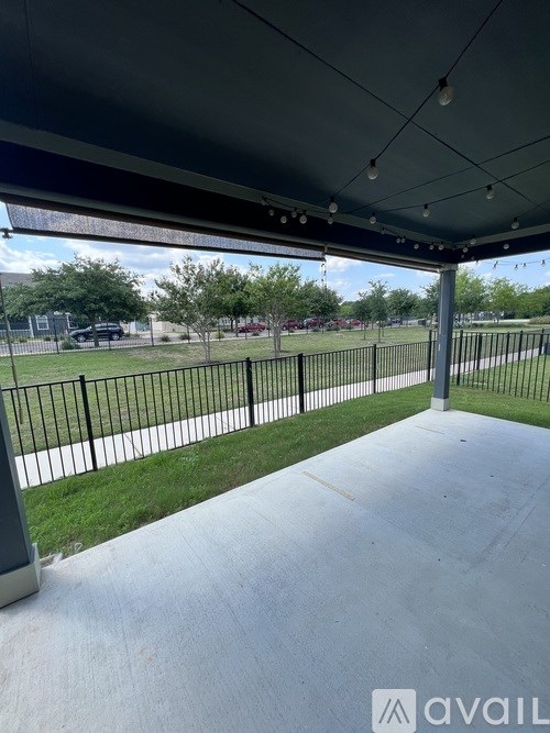 A covered walkway with a view of a grassy area and a fence.