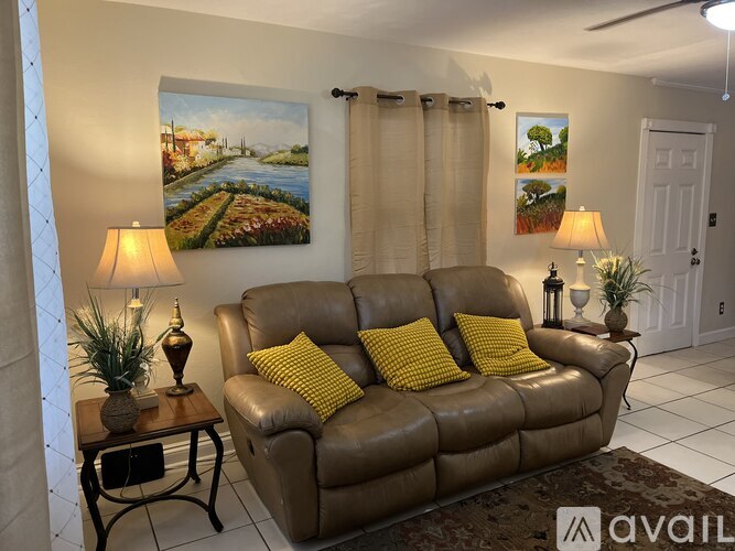 A living room with a brown couch, a painting on the wall, and a small table with a plant on it.