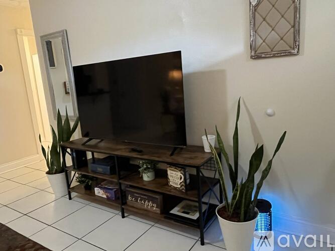 A black television sits on a wooden stand with a plant beside it.