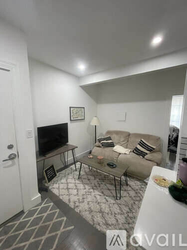 A living room with a grey couch, a black and white rug, and a flat screen TV.