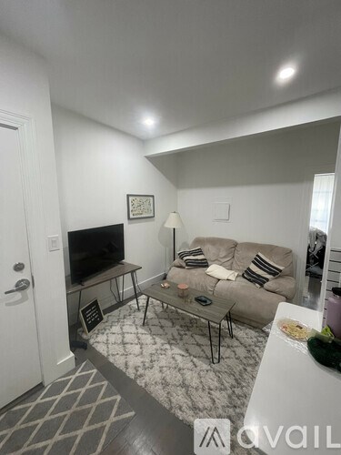 A living room with a grey couch, a black and white rug, and a flat screen TV.
