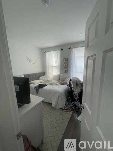 A bedroom with a bed, a television, and a window with curtains.