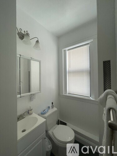 A white bathroom with a toilet, sink, mirror, and window.