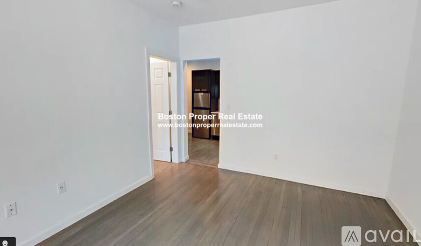 A large empty room with wooden flooring and white walls.