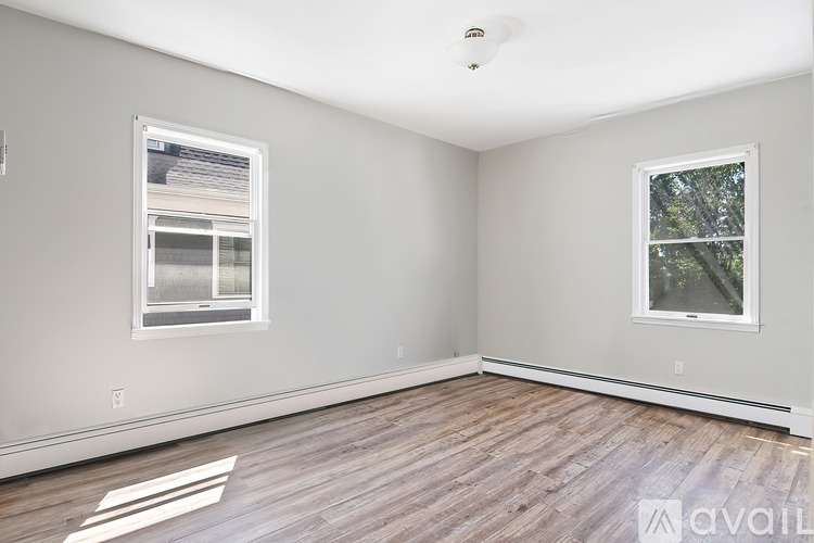 A room with wooden flooring and two windows.