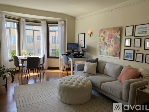 A living room with a grey couch, a white ottoman, a dining table with chairs, and a TV.