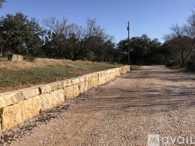 A gravel road with a stone wall on one side and trees on the other.
