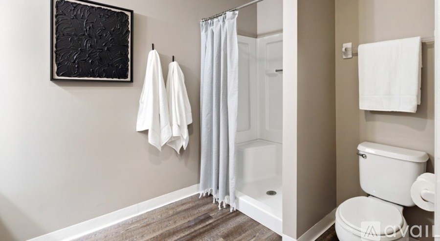 A bathroom with a toilet, a shower with a white curtain, and towels hanging on the wall.