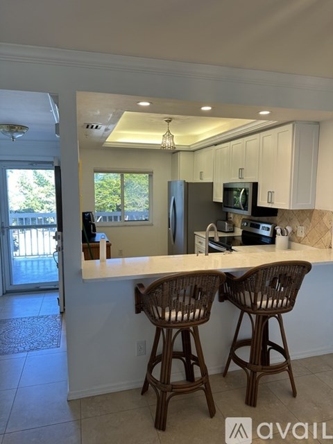 A kitchen with white cabinets and a countertop with two chairs.