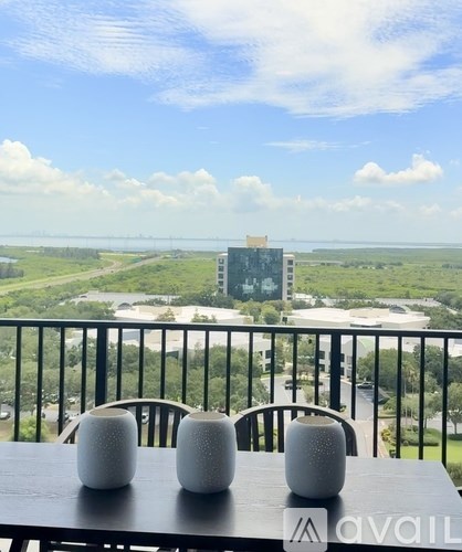 Two white vases sit on a table with a view of a green landscape and buildings in the distance.