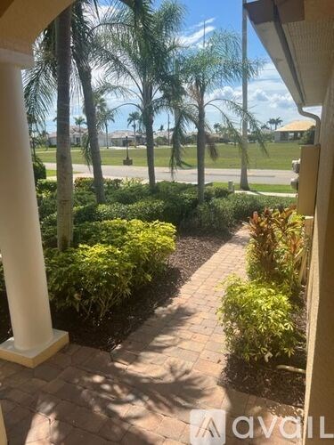 A patio with a white pillar and a view of a street with cars and palm trees.