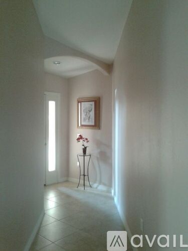 A hallway with a painting on the wall and a vase of flowers on a small table.