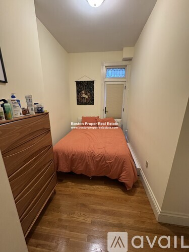 A bedroom with a bed covered in an orange sheet and a wooden dresser.