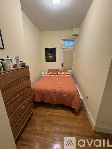 A bedroom with a bed covered in an orange sheet and a wooden dresser.