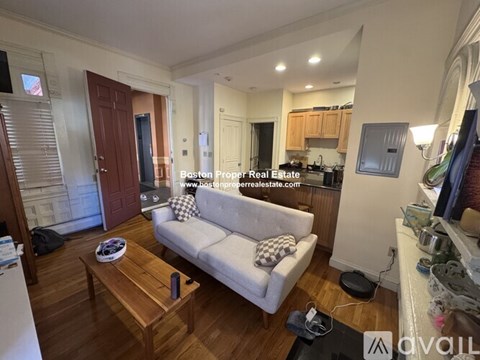 A living room with a couch, coffee table, and kitchen area in the background.