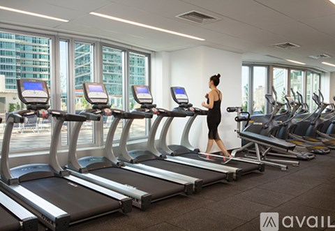 A woman is running on a treadmill in a gym with other treadmills and exercise equipment.