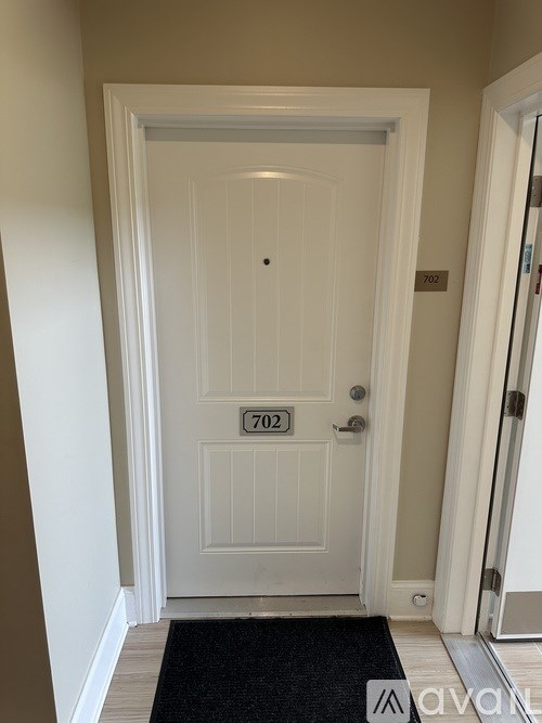 A white door with a black doormat and a number 702 on it.