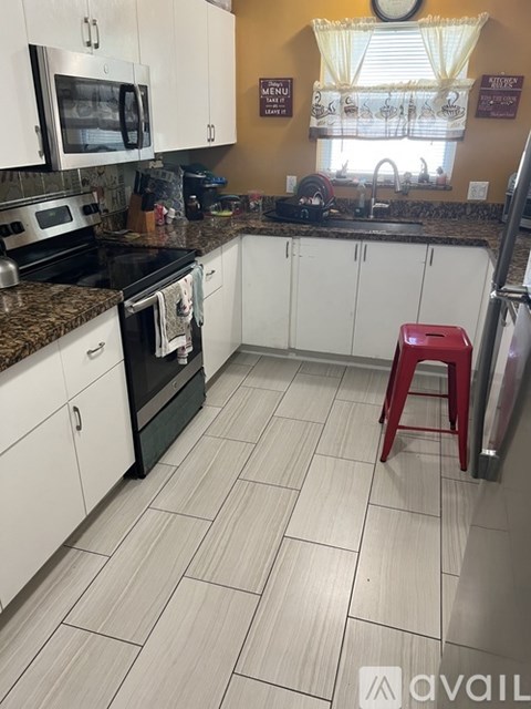 A kitchen with white cabinets and a red stool.