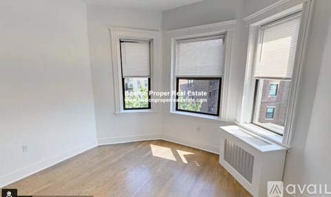 A room with wooden flooring and two windows, one of which has blinds.