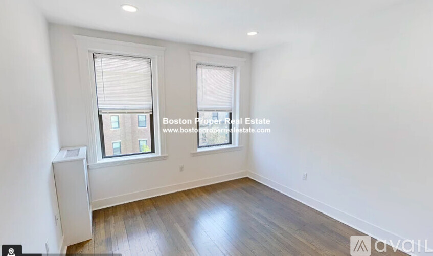 A room with wooden floors and two windows, one of which has a view of a building outside.