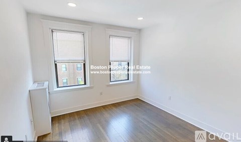 A room with wooden floors and two windows, one of which has a view of a building outside.