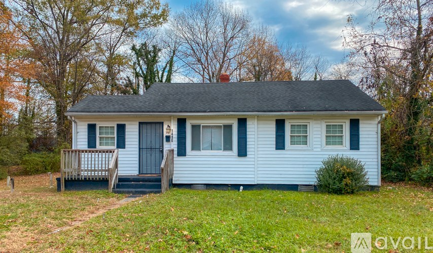 A small blue house with a porch and a tree in the background.