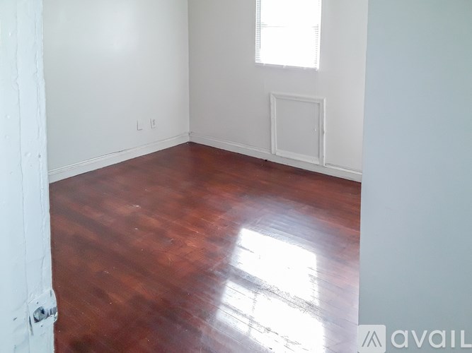 A room with wooden flooring and a window letting in sunlight.