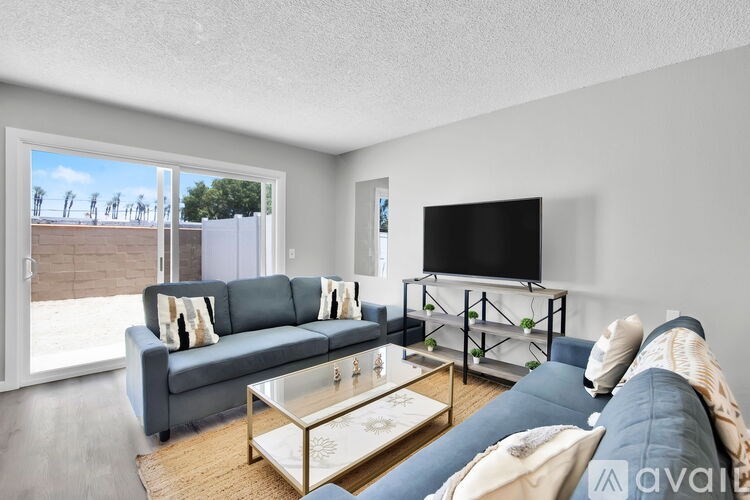 A living room with a grey couch, a glass coffee table, and a flat screen TV mounted on the wall.