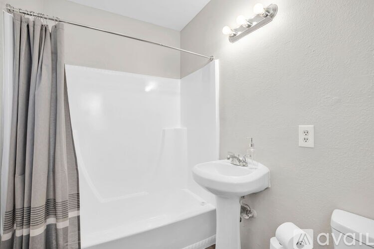 A white sink is on a stand in a bathroom with a white tub and grey curtains.