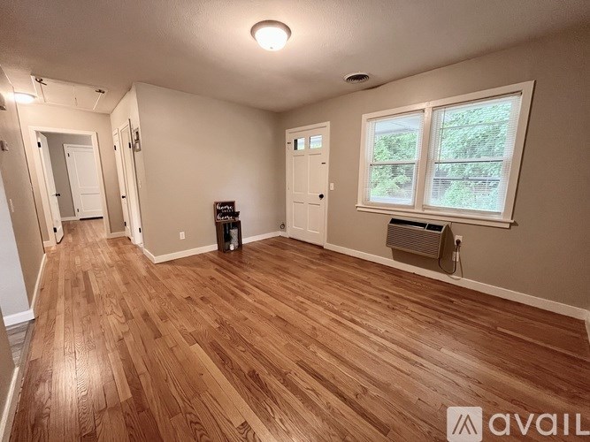 A room with wooden flooring and a window showing greenery outside.