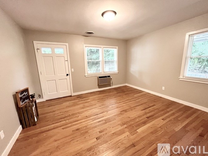A room with wooden flooring and a window showing trees outside.