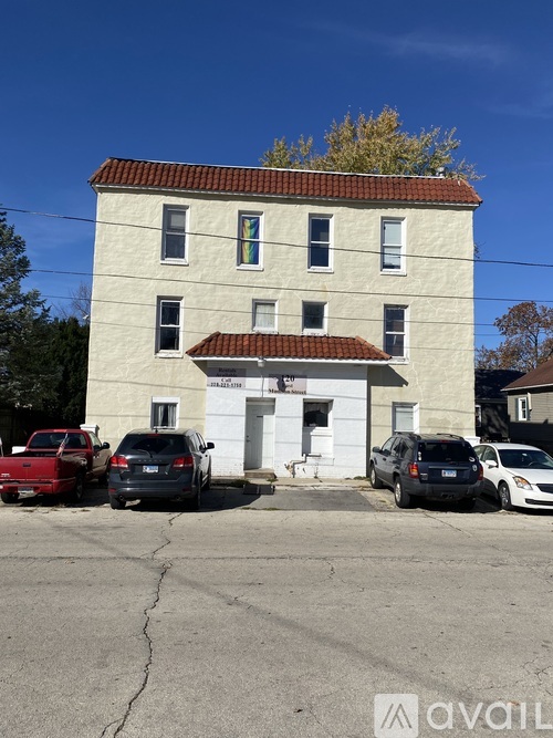 A white building with a red roof and a parking lot in front.