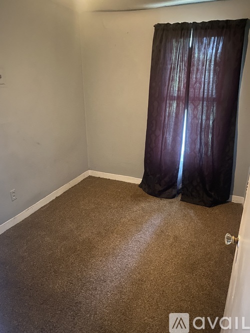 A room with a brown carpet and a curtain.