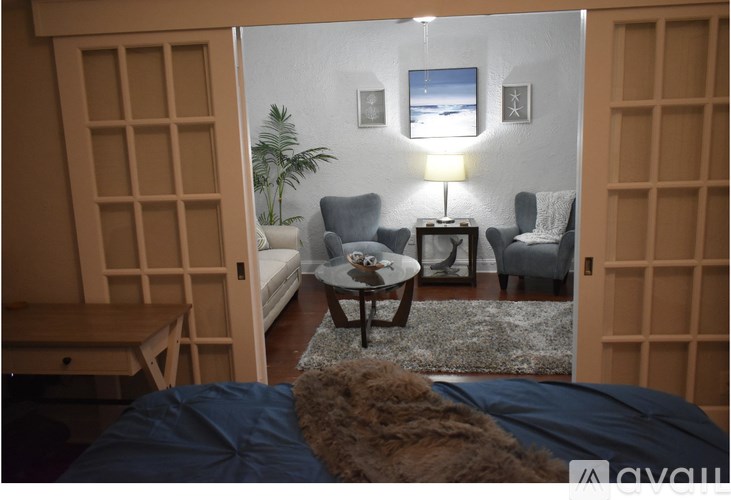 A room with a bed, a chair, a table, and a lamp.