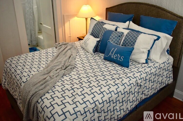 A bed with a white and blue patterned comforter and matching pillow cases with the word "Hers" written on them.