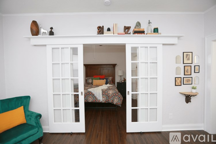 A room with a white doorway leading to a bedroom, a green chair, and a shelf with various objects on it.