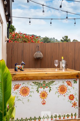 A wooden table with a floral design is in front of a wooden fence.