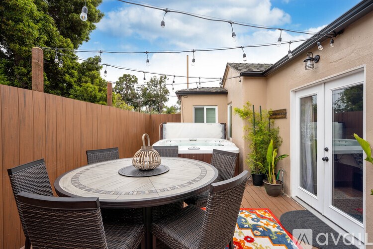 A patio with a round table surrounded by chairs and a hot tub in the background.