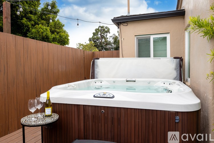 A hot tub is on a deck with a bottle of wine and a glass on the side table.