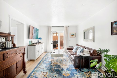 A living room with a brown leather couch and a blue rug.