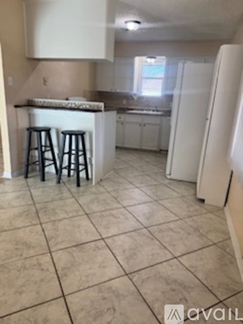 A kitchen with a white refrigerator and a bar with stools.