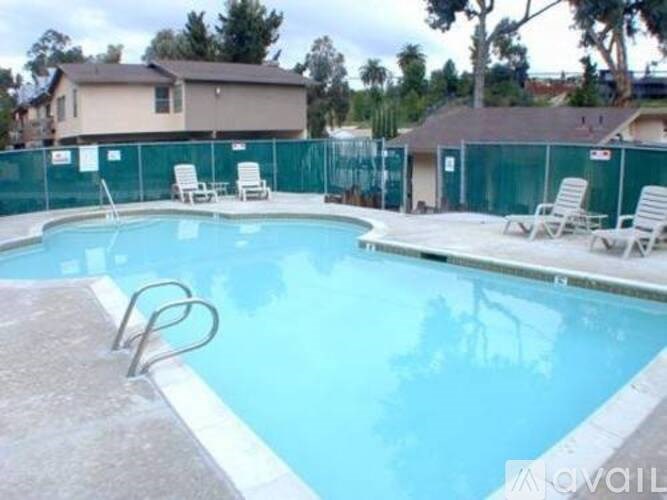 A pool with chairs around it and a fence in the background.