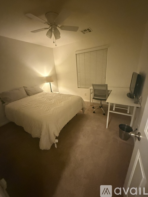A bedroom with a bed, desk, chair, and a ceiling fan.
