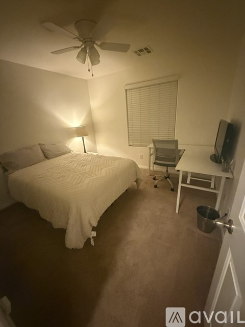 A bedroom with a bed, desk, chair, and a ceiling fan.