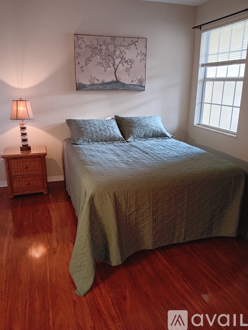 A bedroom with a bed, a nightstand with a lamp, and a painting on the wall.