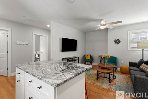 A kitchen with a marble countertop and a living room with a couch and a chair.